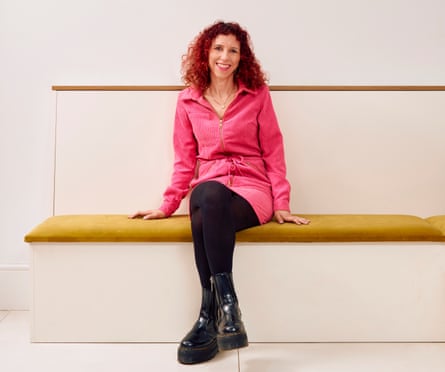Writer Serena Kutchinsky, in pink dress and black boots, sitting on a padded bench