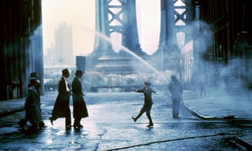An expansive image in blue hues, of men in long black coats and hats crossing a damp street toward a boy in a newsboy hat, amid steam rising from the street beneath a bridge in New York City.