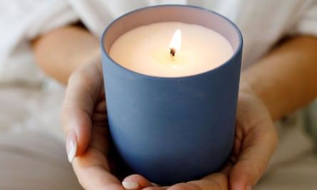 A lit candle in a blue ceramic vessel cupped in two hands.