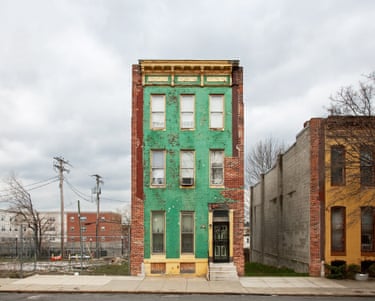 A tall green row house, next to an area of fenced waste ground