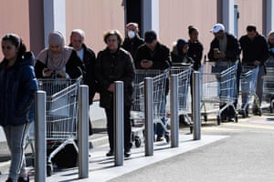 A woman wears a protective facemask she pushes a shopping trolley as she queues to enter in a supermarket in Hnheim, northeastern France on Monday