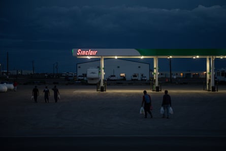 Men walk past a petrol station at dusk