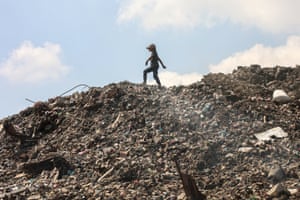 A girl walks on a high ridge of a huge pile of rubbish
