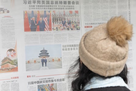 a person in a woolly hat reads a newspaper displayed on a wall