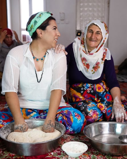 Demir sits on the floor with her hands in a bowl of dough, next to an older woman.