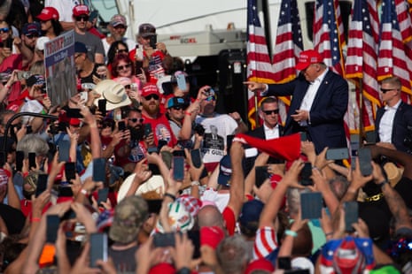 Donald Trump points toward a crowd holding up phones and signs at a campaign rally
