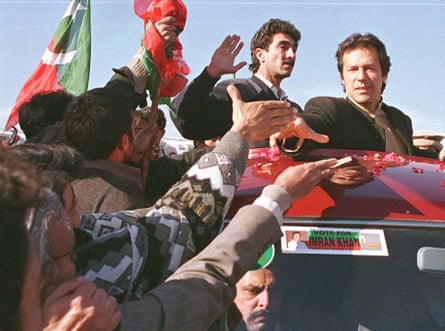 Pakistani youths reach out to Imran Khan who is standing up in an open top car.