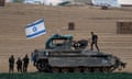 Five Israeli soldiers – three stood on the ground and two on the vehicle - with an armoured personnel carrier that is flying the Israeli flag