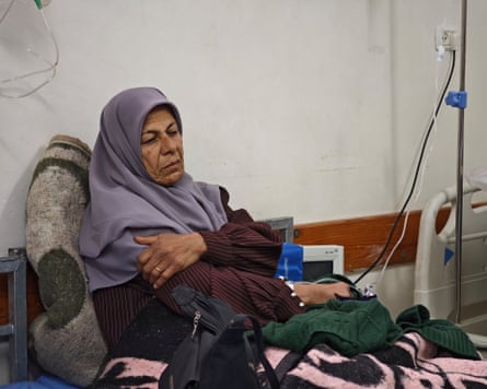 A woman wearing a headscarf sits on a hospital bed attached to a drip