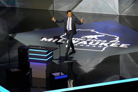 man walks onstage toward podium with arms out