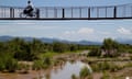 Man cycling across a bridge over a river in desert landscape in Mexico.