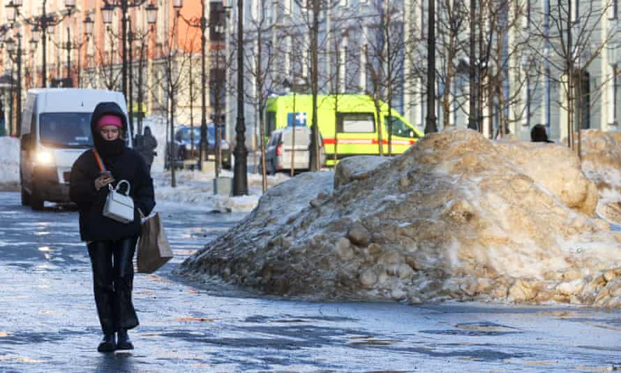 A woman in a black coat walks past piles of melting snow on Malaya Konyushennaya Street in St Petersburg, Russia on 12 January. The city recorded a daily record of new Covid cases on Wednesday.