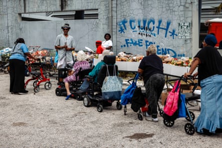 a group of elderly people in walkers and wheelchairs wait in line at a food bank
