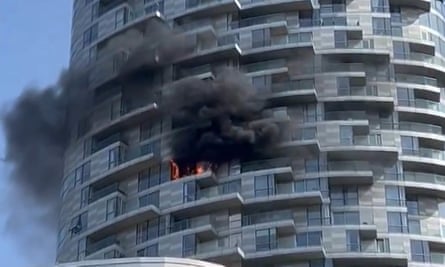 Black smoke billows out of the side of circular-shaped tower block