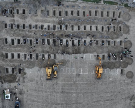 Rows of many graves being dug by a mechanical digger, seen from the air