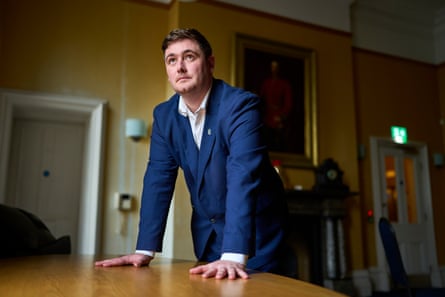 Chris Cooke leans on a table, looking up, in his office
