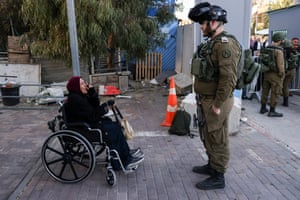 A woman in a wheelchair gestures with her hand as she faces an Israeli soldier who stands with his hands in his pockets