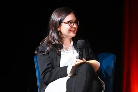 a woman seated on stage smiles while holding a microphone