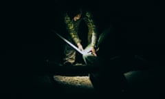 A soldier wearing a headlamp crouches over a drone in the dark