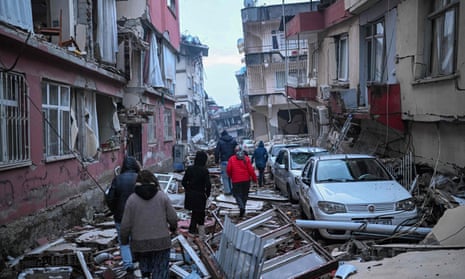 People walk along a street strewn with debris as they look for relatives in Hatay.