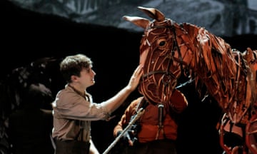 Seth Numrich with his hand resting on the head of a giant puppet horse.