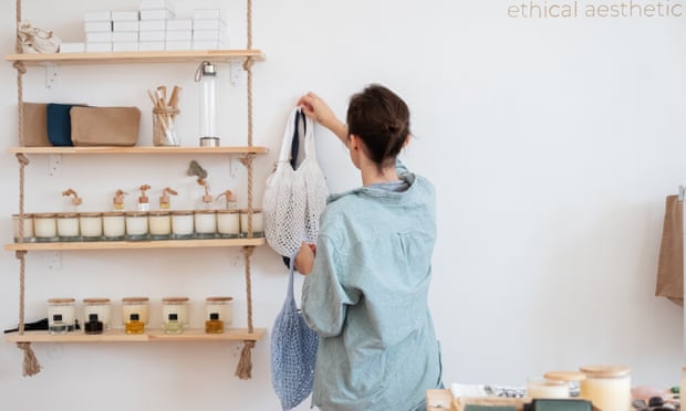 Back view of woman in casual clothes hanging zero waste sacks on wall near shelves with organic cosmetic in eco friendly shop.