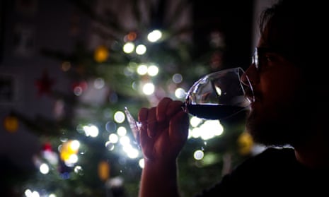 A man drinks a glass of wine by a Christmas tree.