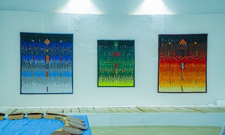 Multicoloured art on the wall of a gallery with a sculpture also on show that seems to be made of giant coins