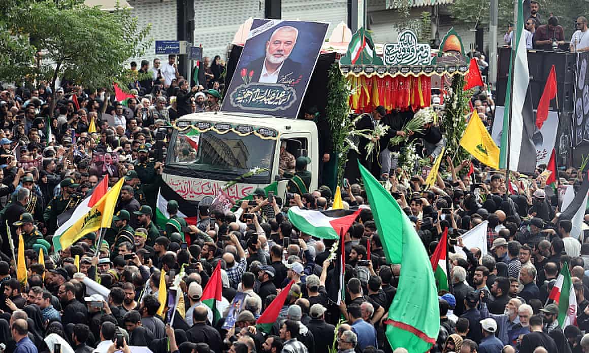 People, some waving flags, crowd around a flatbed truck carrying the coffin of Ismail Haniyeh. A large picture of him is placed on the roof of the truck's cab