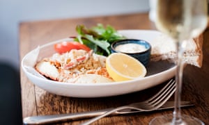 Seafood dish served with half a lemon and sauce, plus a glass of white wine on a table in the dining area the Castle Inn, West Lulworth, Dorset.