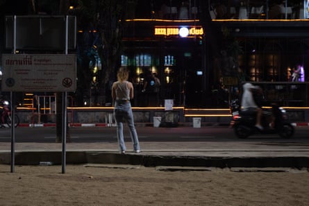 A woman stands on the sidewalk at night by Pattaya Beach.