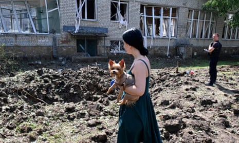 A woman holding a dog stands by a crater from a missile blast next to a destroyed school building in Kharkiv.