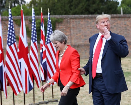 Donald Trump speaks to unseen listeners over his shoulder while he grips Theresa May’s arm as they walk past UK and US flags