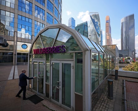 A man enters a glass building with the Wildberries logo above the door. Parts of the Moscow skyline are visible in the background