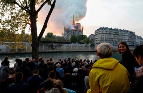 Bystanders look on as flames and smoke billow from the roof at Notre Dame Cathedral in Paris.