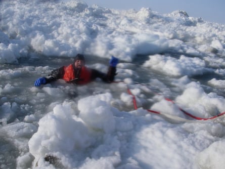 An explorer flounders in the sea, surrounded by ice, hanging on to a red rope