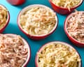 Several red-rimmed bowls filled with creamy coleslaw in varying colors sit on a turquoise surface