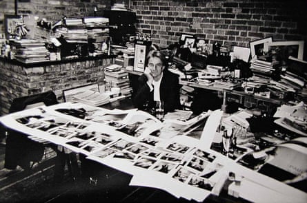 A black and white photograph shows Smith sitting down, surrounded by desks that are covered in photos and books.