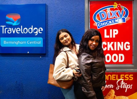 Two girls with dark hair walking past a Travelodge sign and a Dixy Chicken Lip Licking Food sign