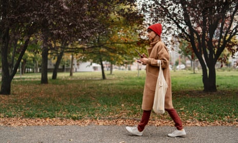 A woman in autumnal colours carrying dangling tote bag walking in the park.