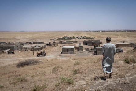 A man stands on a dry hillside looking at a small settlement