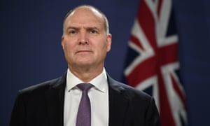 man in dark suit and tie with the australian flag hanging behind him