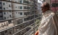 An elderly man with glasses on a balcony overlooking a city street in Dhaka