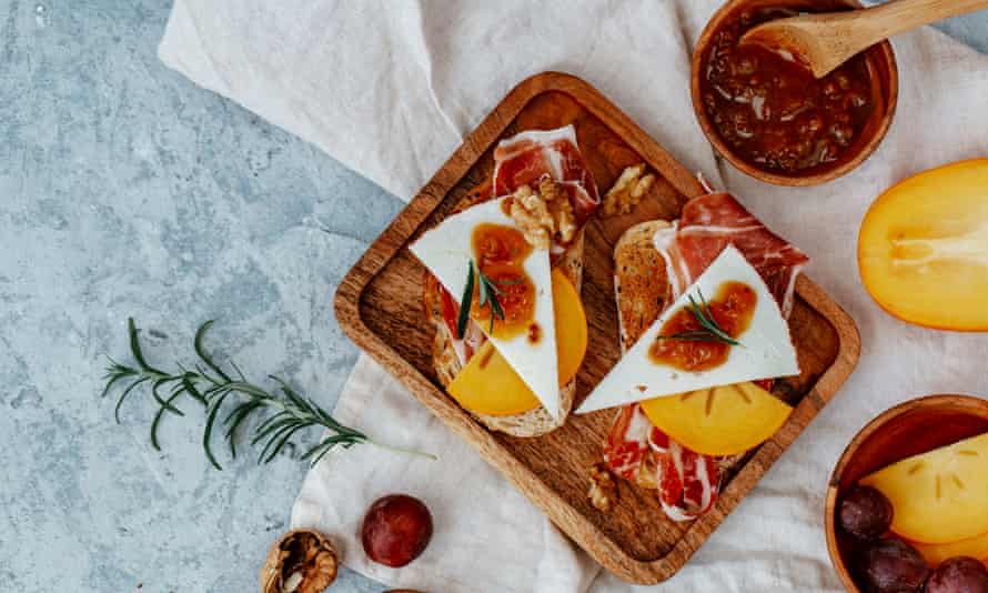 Overhead view of two slices of toast with serrano ham, cheese, persimmon and chutneyGettyImages-1321106797