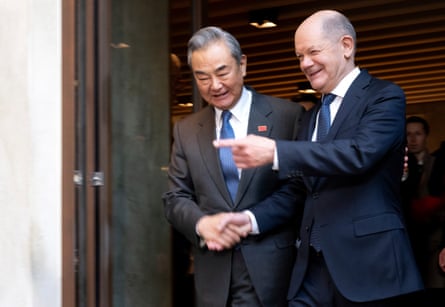Germany’s chancellor, Olaf Scholz, clasps hands with China’s foreign minister, Wang Yi