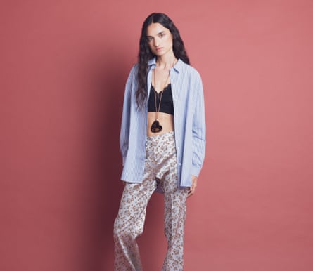A model in an open blue shirt, black bralette and floral-pattern satin trousers with a heart-shaped pendant A model in an open blue shirt, black bralette and floral-pattern satin trousers with a heart-shaped pendant