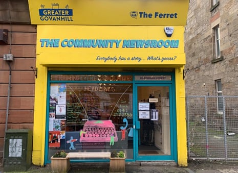 An inviting-looking shopfront painted in yellow and turquoise, with a large glass window. A sign at the top reads: 'The Community Newsroom', with the strapline: 'Everybody has a story ... what's yours?'. Above this are the Greater Govanhill and Ferret logos. The large window features a hand-drawn pink typewriter and the word 'headlines' above it, and there are various notices pinned in the window too.