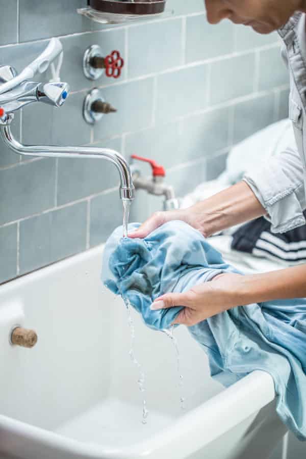 A person partially washing a blue blouse by hand