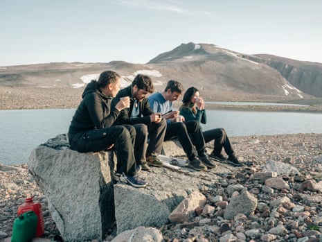 four people sitting on a rock with water behind them