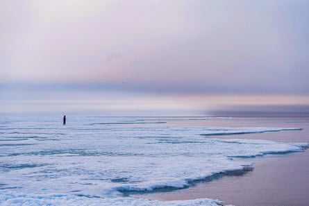 A distant figure standing on an ice floe near where it meets open water